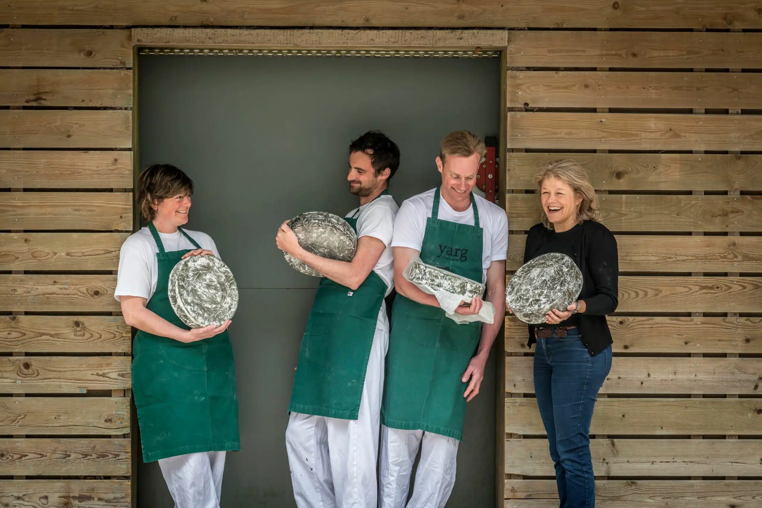 Lynher Dairies staff holding wheels of their cheese laughing.