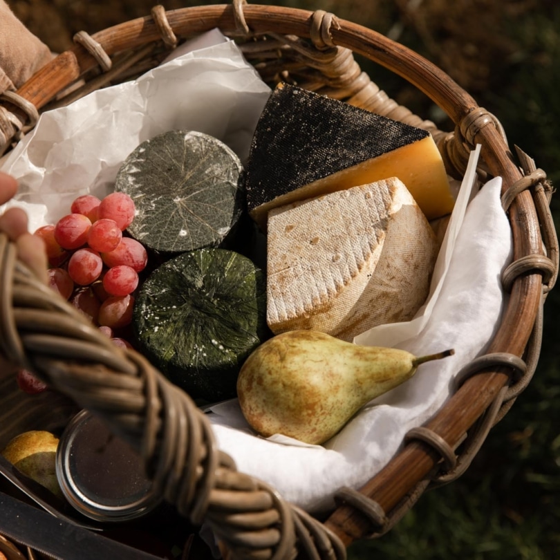 A basket containing various cheeses and fruit.